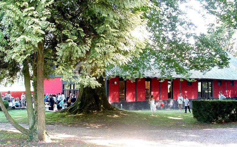 Un bâtiment rouge entouré d'arbres, avec des personnes rassemblées à l'extérieur sur une pelouse.