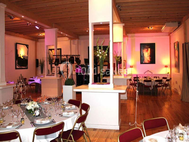Salle de réception lumineuse avec tables dressées, chaises rouges, décorations florales et œuvres d'art aux murs.