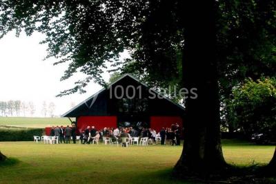 Terrasse en bois longeant un bâtiment en briques avec vue sur un jardin arboré sous un ciel bleu.