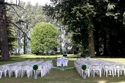 Terrasse en bois longeant un bâtiment en briques avec vue sur un jardin arboré sous un ciel bleu.