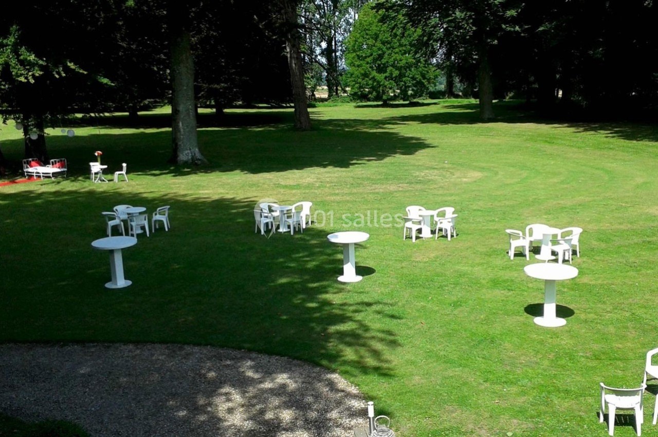 Tables et chaises blanches disposées sur une pelouse verdoyante, entourées d'arbres dans un espace extérieur.