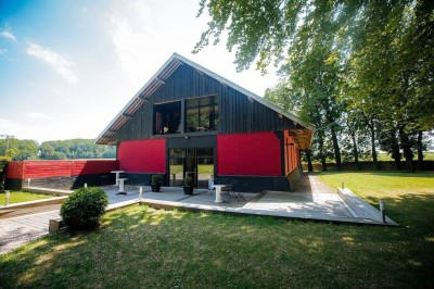 Terrasse en bois longeant un bâtiment en briques avec vue sur un jardin arboré sous un ciel bleu.