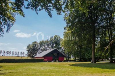 Terrasse en bois longeant un bâtiment en briques avec vue sur un jardin arboré sous un ciel bleu.