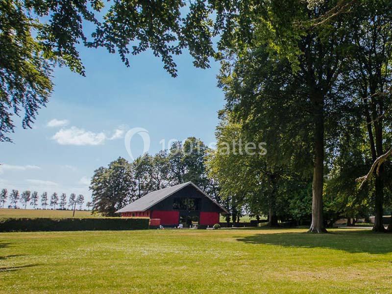 Une grande maison rouge entourée d'arbres dans un paysage verdoyant sous un ciel bleu clair.