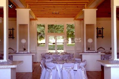 Terrasse en bois longeant un bâtiment en briques avec vue sur un jardin arboré sous un ciel bleu.