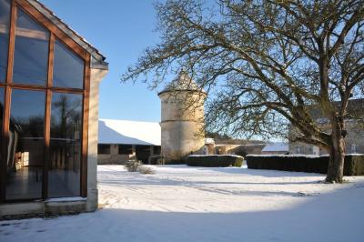 Cour enneigée avec bâtiments en pierre, un pigeonnier cylindrique et des arbres nus sous un ciel dégagé.
