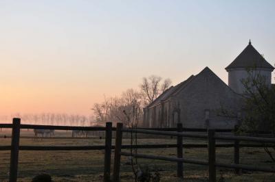 Cour enneigée avec bâtiments en pierre, un pigeonnier cylindrique et des arbres nus sous un ciel dégagé.