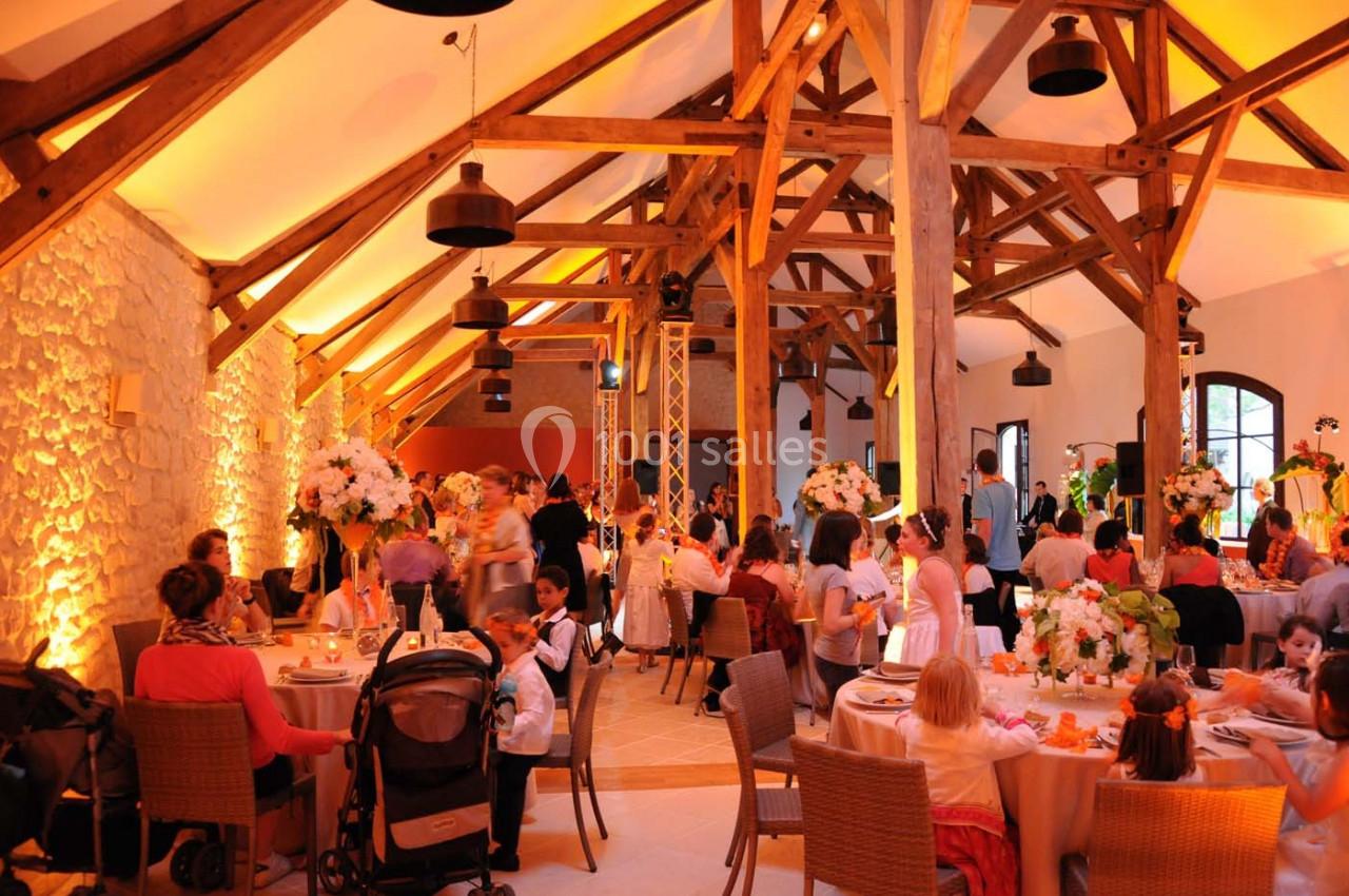Salle de réception avec des poutres apparentes, décorations florales et invités assis autour de tables rondes.