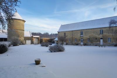 Cour enneigée avec bâtiments en pierre, un pigeonnier cylindrique et des arbres nus sous un ciel dégagé.
