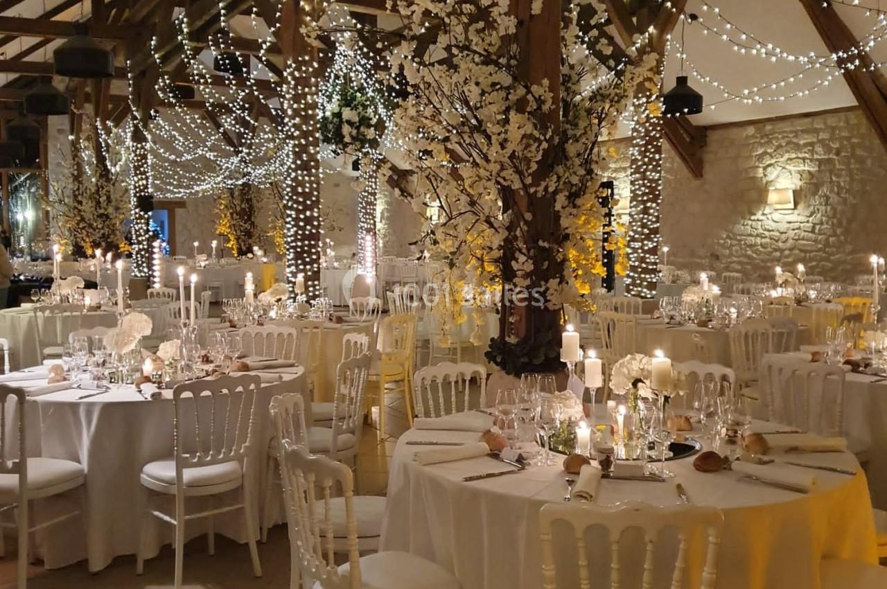 Salle de réception décorée pour un mariage, avec tables dressées, guirlandes lumineuses et arbres fleuris.