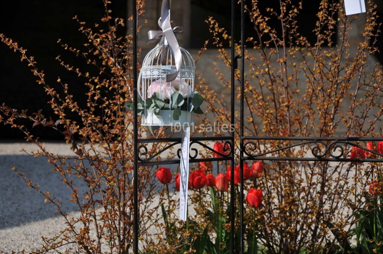 Cage décorative blanche suspendue, contenant des fleurs, devant des tulipes rouges et des branches fleuries.