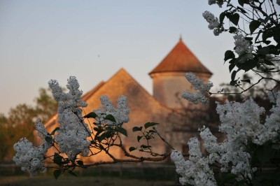 Cour enneigée avec bâtiments en pierre, un pigeonnier cylindrique et des arbres nus sous un ciel dégagé.