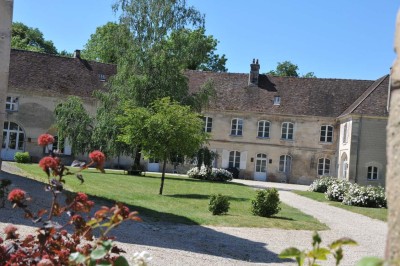 Cour enneigée avec bâtiments en pierre, un pigeonnier cylindrique et des arbres nus sous un ciel dégagé.