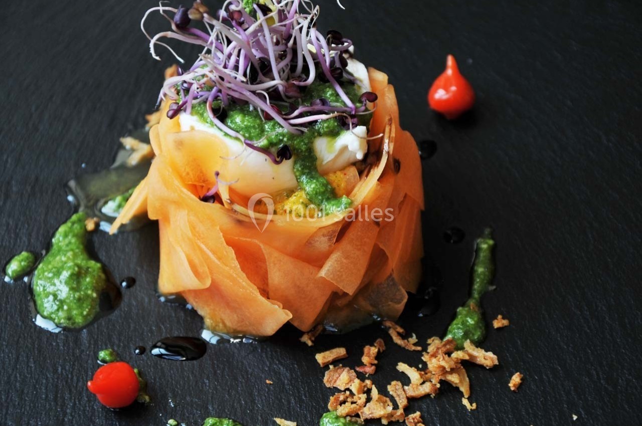 Assiette gastronomique avec légumes en rubans, œuf poché, pousses germées, pesto et éclats croustillants sur ardoise noire.