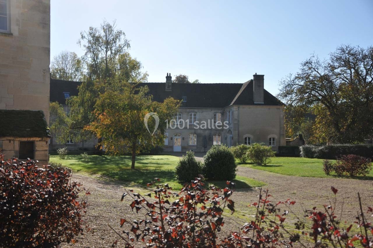 Façade d'un bâtiment en pierre entouré d'un jardin arboré, sous un ciel dégagé.