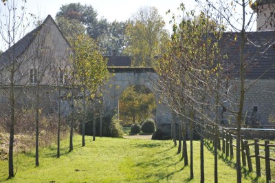 Cour enneigée avec bâtiments en pierre, un pigeonnier cylindrique et des arbres nus sous un ciel dégagé.
