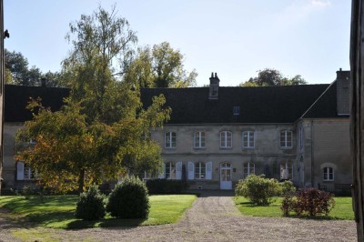 Cour enneigée avec bâtiments en pierre, un pigeonnier cylindrique et des arbres nus sous un ciel dégagé.