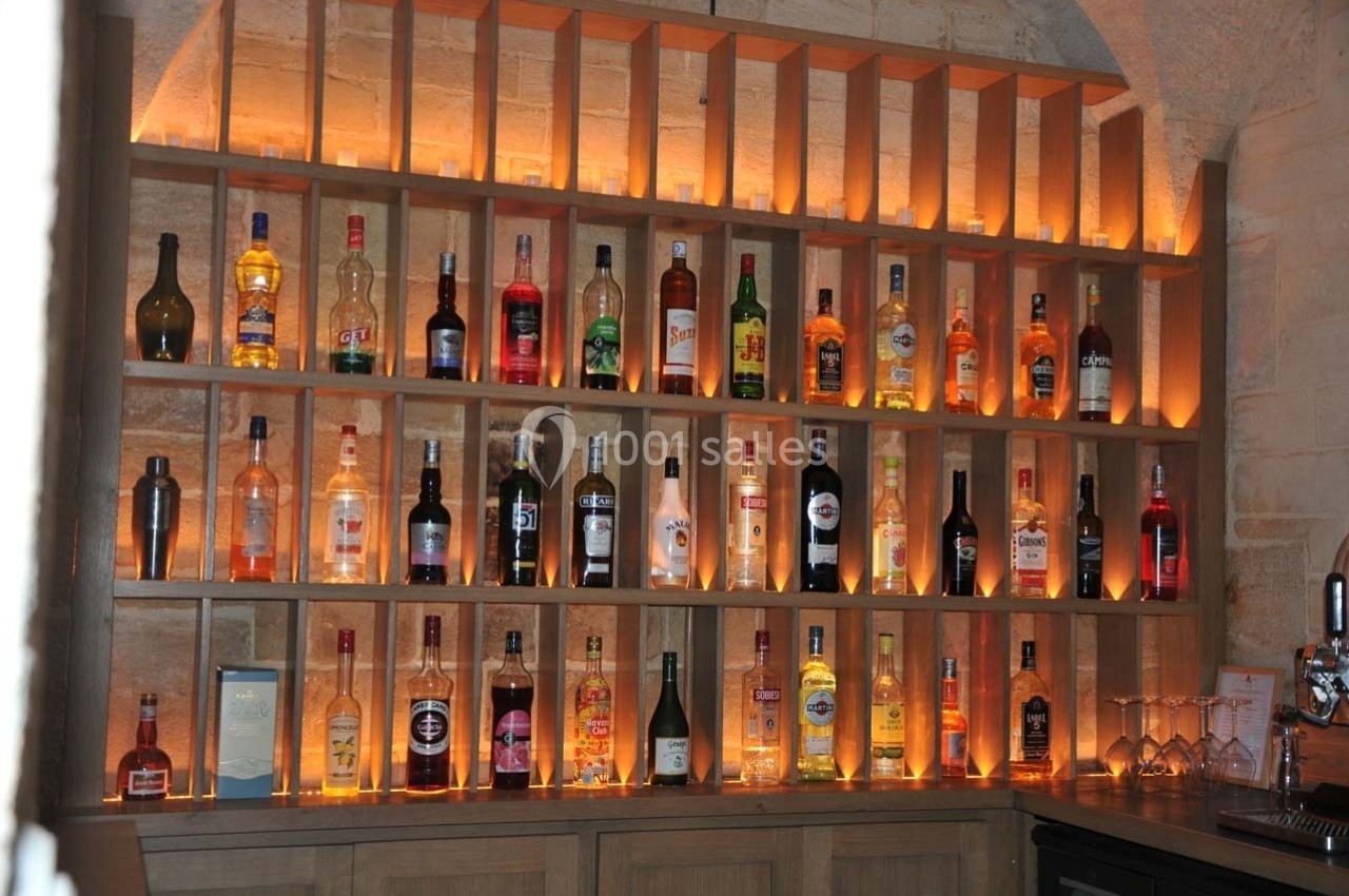 Étagères en bois éclairées contenant diverses bouteilles d'alcool dans un bar à l'ambiance chaleureuse.