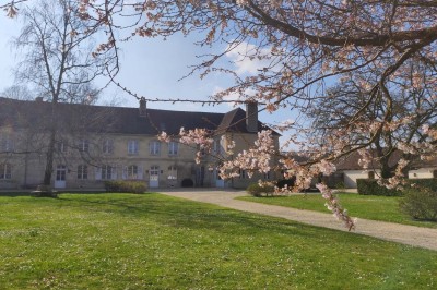 Cour enneigée avec bâtiments en pierre, un pigeonnier cylindrique et des arbres nus sous un ciel dégagé.