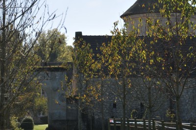 Cour enneigée avec bâtiments en pierre, un pigeonnier cylindrique et des arbres nus sous un ciel dégagé.