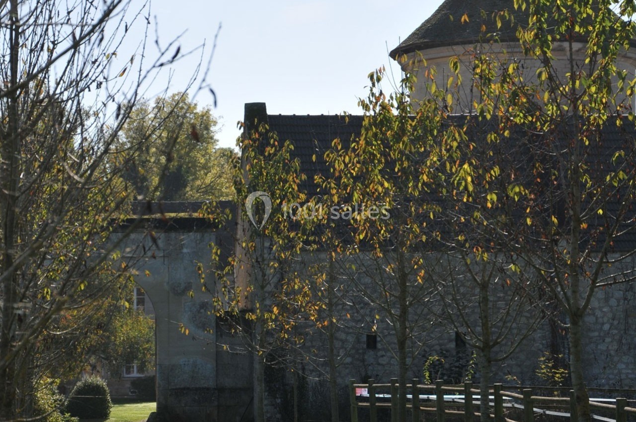 Vue d'un mur en pierre avec un porche, entouré d'arbres aux feuilles d'automne sous un ciel clair.