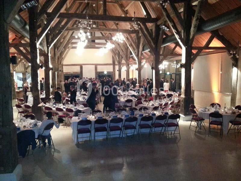 Salle de réception en bois avec des tables dressées et des invités rassemblés pour un événement.