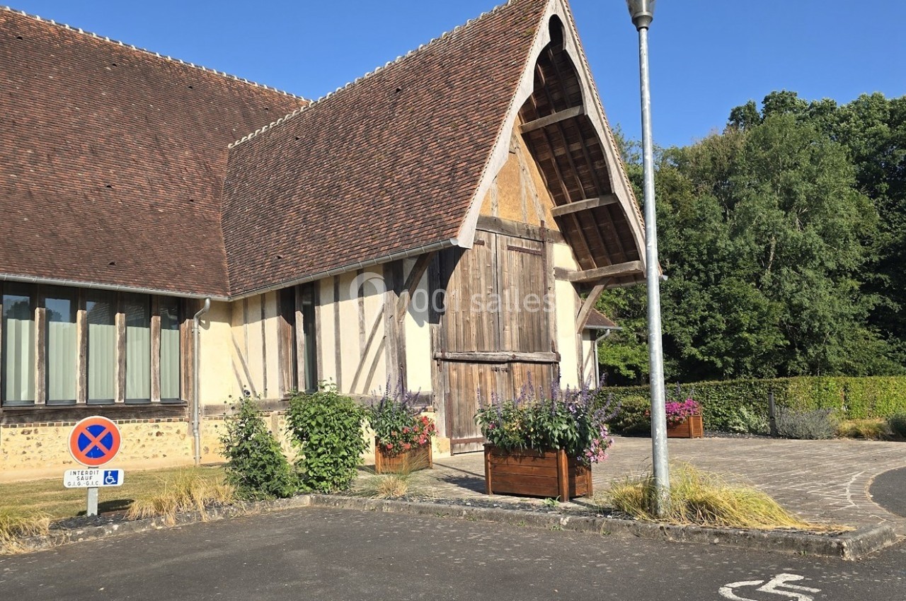 Bâtiment à colombages avec toit en tuiles, parking avec panneau d'interdiction et végétation environnante.