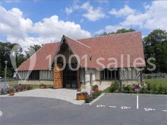 Salle de réception avec rangées de chaises rouges alignées sous une charpente en bois apparente.