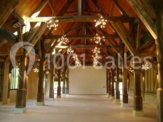 Charpente en bois apparente dans une grande salle avec plafond haut, éclairée par des lustres suspendus.