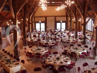 Salle de réception avec rangées de chaises rouges alignées sous une charpente en bois apparente.