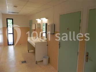 Salle de toilettes avec deux lavabos, miroirs, distributeurs de savon et portes vertes, éclairée par une fenêtre.