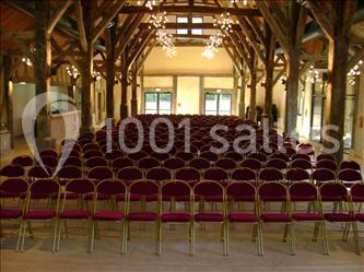 Salle de réception avec rangées de chaises rouges alignées sous une charpente en bois apparente.