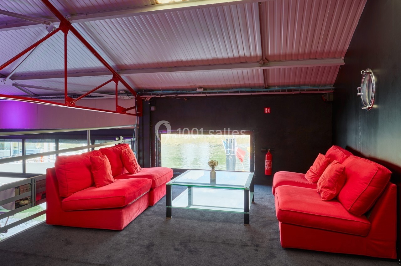 Location salle Paris 15 (Paris) - Paris Yacht Marina #16 Deux canapés rouges autour d'une table basse en verre dans un espace intérieur avec vue sur l'extérieur par une fenêtre.