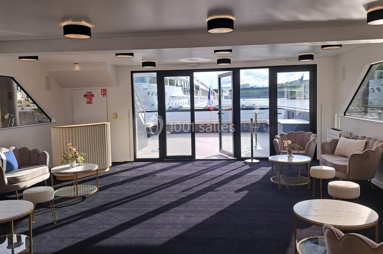 Location salle Paris 15 (Paris) - Paris Yacht Marina #18 Salon lumineux avec fauteuils, tables basses et grandes baies vitrées donnant sur un quai et un bateau amarré.