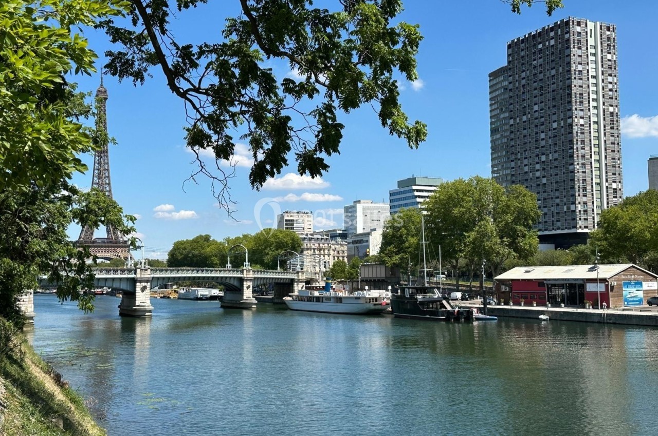 Vue d'un canal à Paris avec un pont, des péniches, des immeubles modernes et la tour Eiffel en arrière-plan.