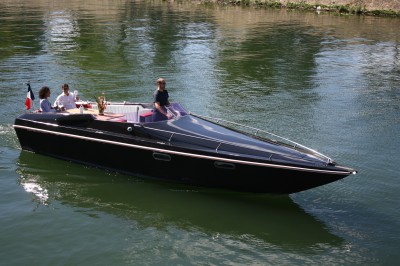 Bateaux amarrés le long d'un quai sur une rivière, avec une promenade bordée d'arbres à gauche.