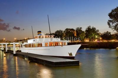 Bateaux amarrés le long d'un quai sur une rivière, avec une promenade bordée d'arbres à gauche.
