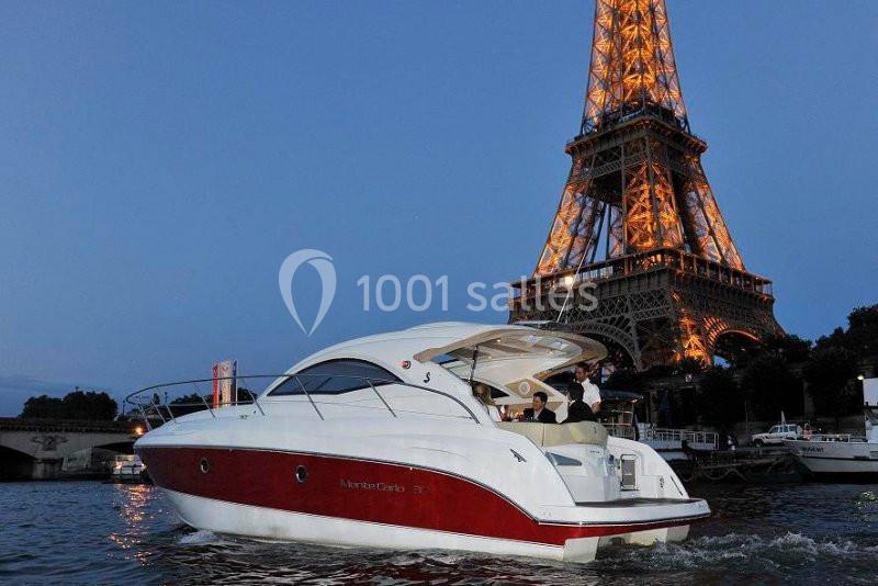 Bateau de plaisance blanc et rouge naviguant sur la Seine, avec la tour Eiffel illuminée en arrière-plan.