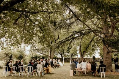 Salle de réception lumineuse avec tables rondes dressées, nappes blanches, chaises en bois et décorations florales.