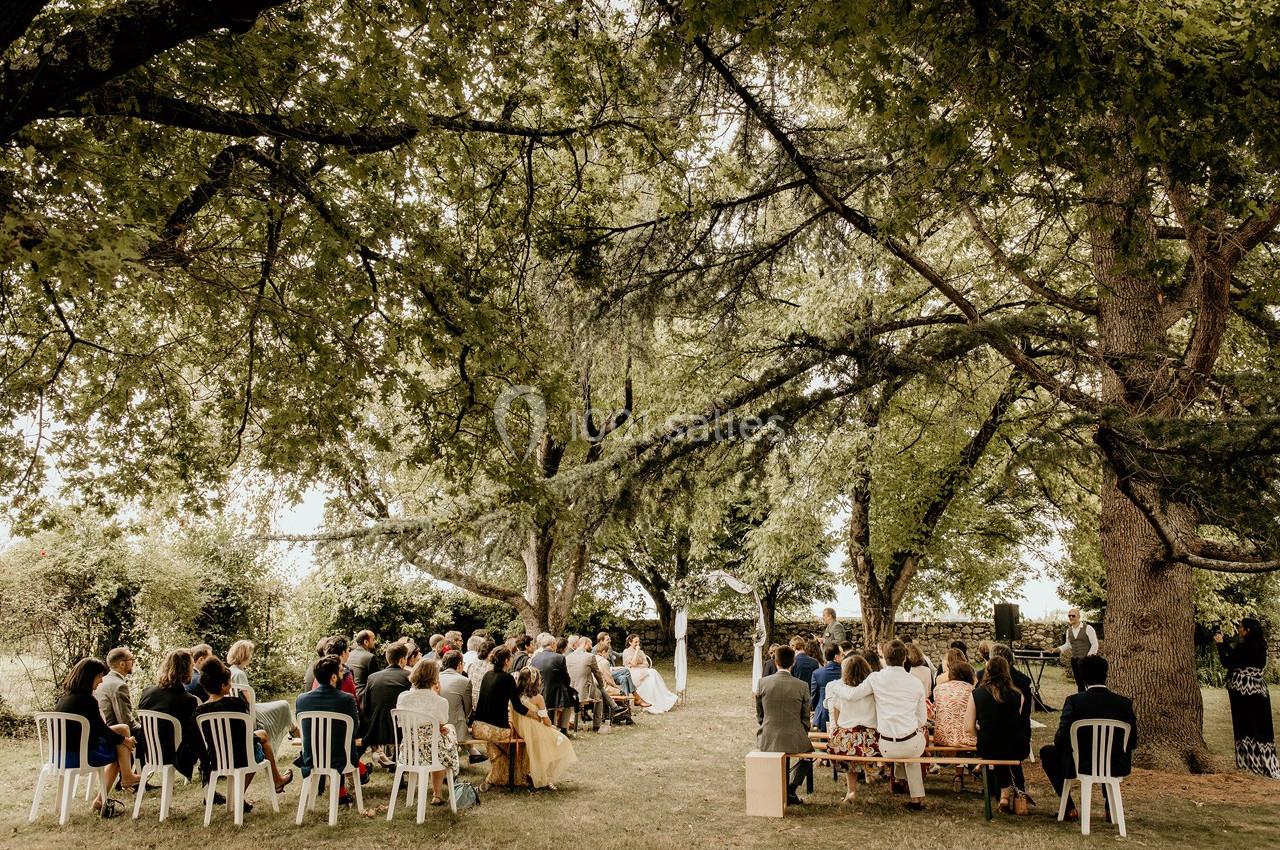 Groupe de personnes assises en extérieur sous de grands arbres lors d'une cérémonie en plein air.