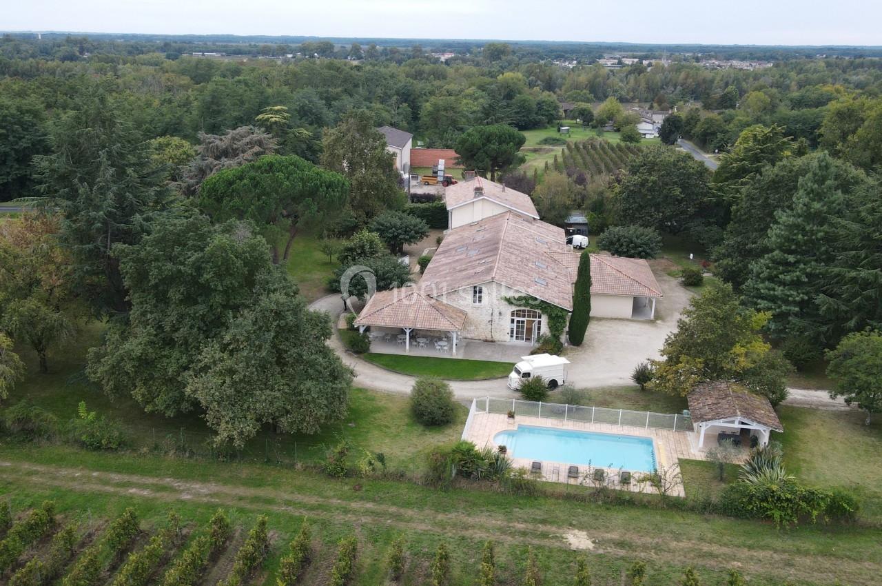 Vue aérienne d'une maison avec toit en tuiles, piscine clôturée, jardin arboré et vignes en arrière-plan.