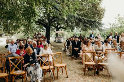 Salle de réception lumineuse avec tables rondes dressées, nappes blanches, chaises en bois et décorations florales.