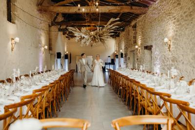 Salle de réception lumineuse avec tables rondes dressées, nappes blanches, chaises en bois et décorations florales.