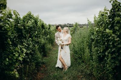 Salle de réception lumineuse avec tables rondes dressées, nappes blanches, chaises en bois et décorations florales.