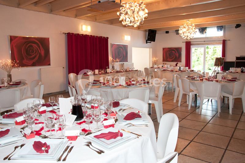 Salle de réception décorée avec des tables rondes dressées, nappes blanches et accents rouges, éclairage chaleureux.