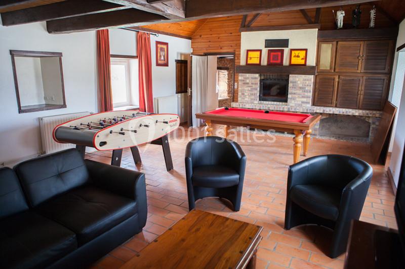 Salle de loisirs avec baby-foot, table de billard, canapés noirs et murs en bois dans un espace lumineux.