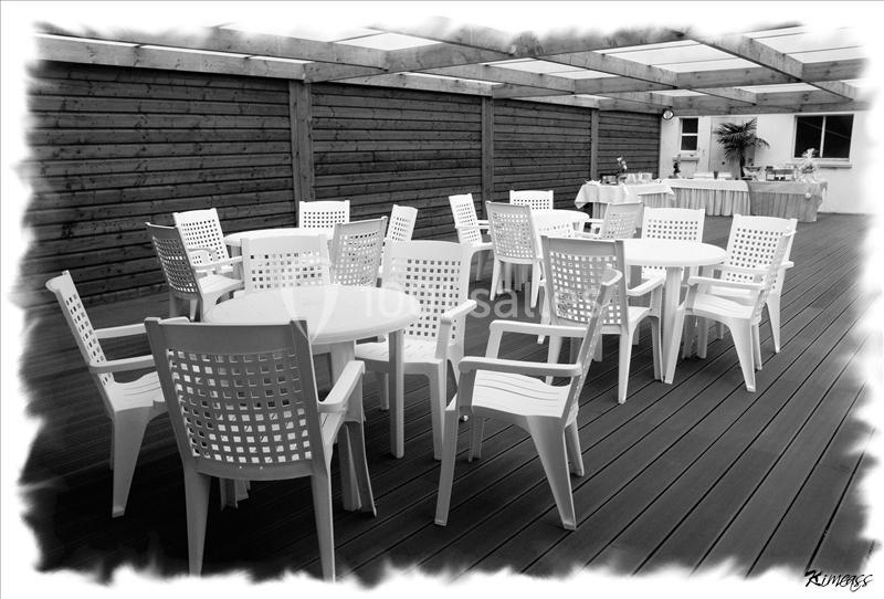 Salle extérieure couverte avec des tables et chaises en plastique blanc disposées sur un sol en bois.
