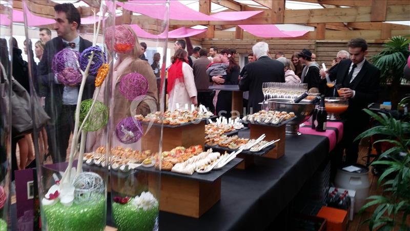 Buffet de réception avec amuse-bouches variés, invités debout en arrière-plan dans une salle décorée.