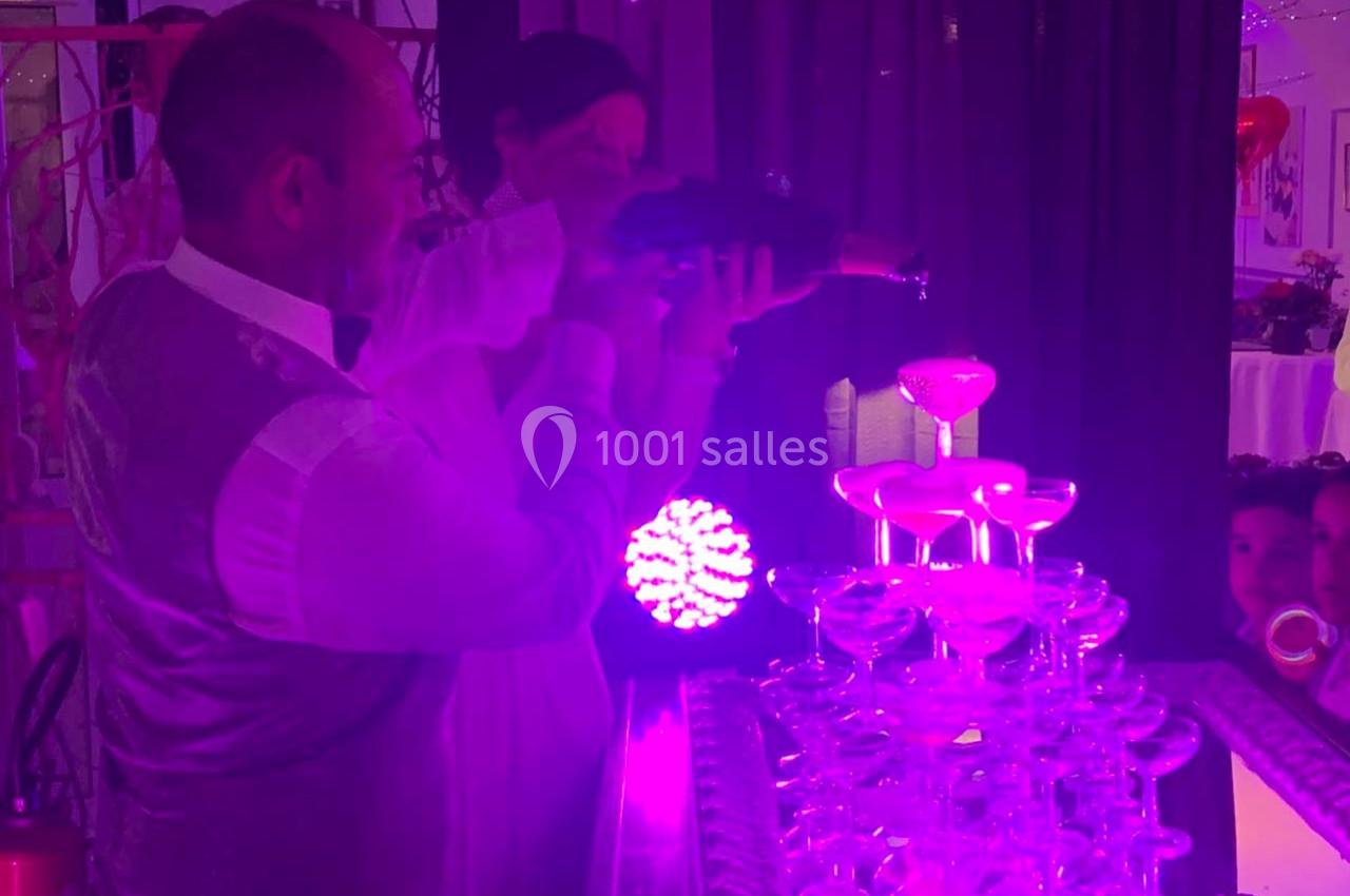 Un serveur verse du champagne dans une pyramide de coupes éclairée par une lumière violette.