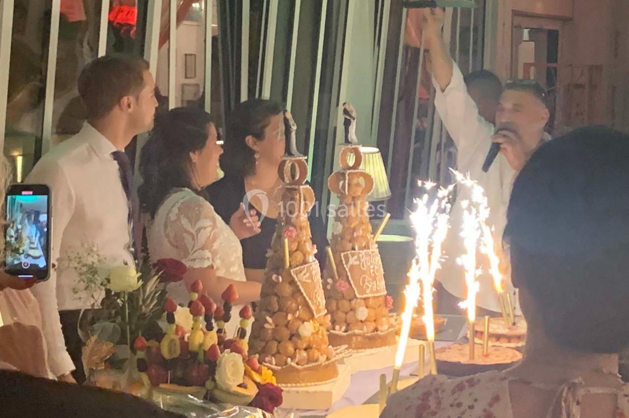 Un groupe de personnes autour de pièces montées et desserts, avec des étincelles et un animateur parlant au micro.